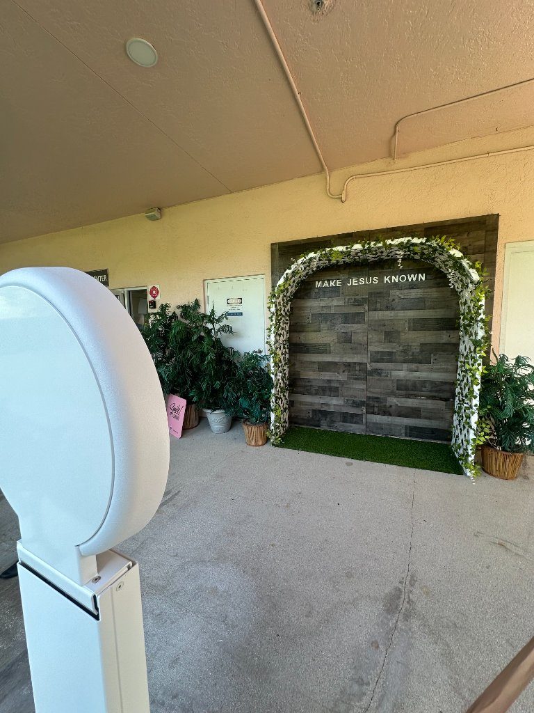 White photo booth staged beside a greenery arch